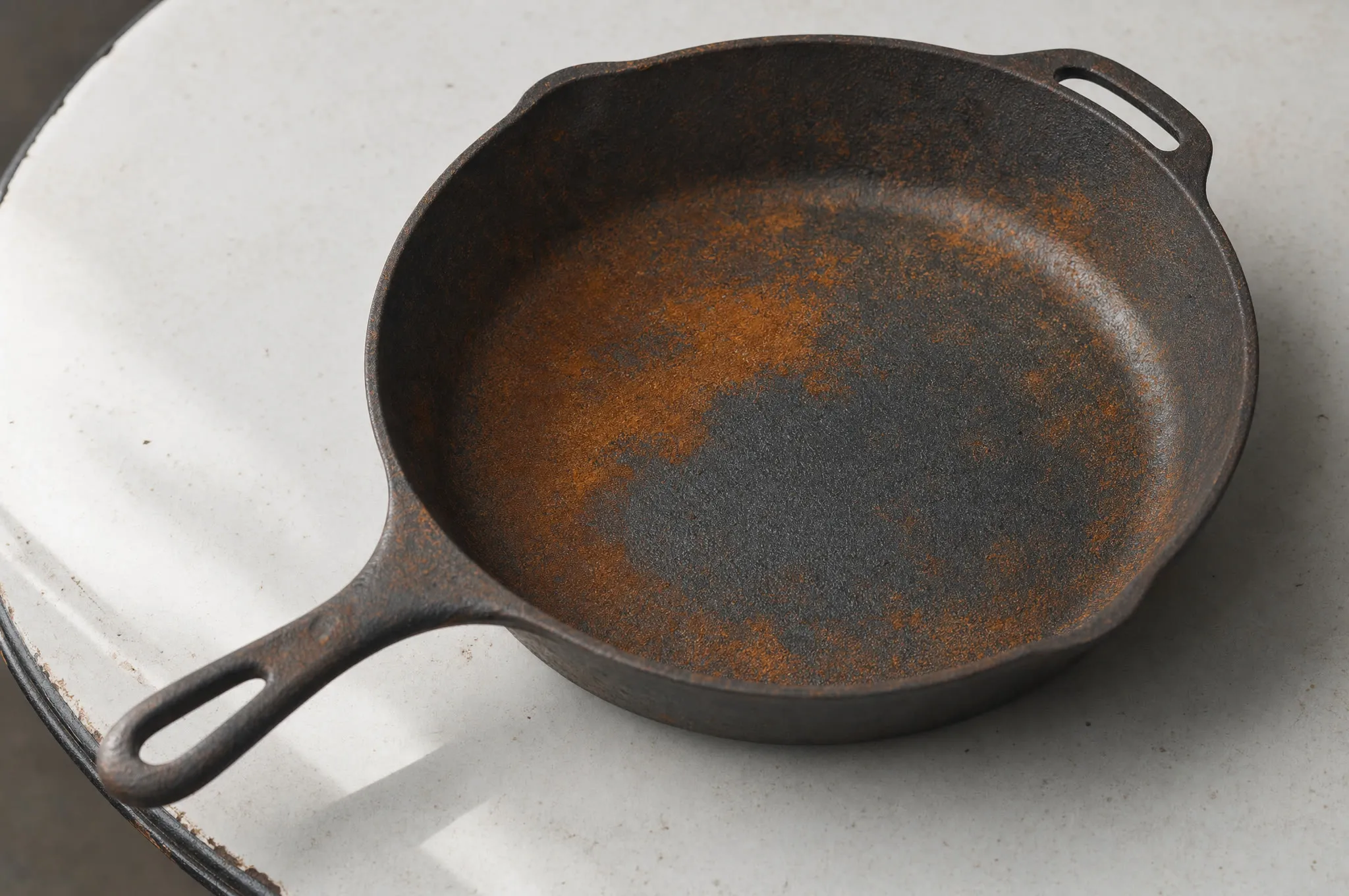 Moderately rusted vintage cast iron skillet on a white enamel table, patchy orange surface rust